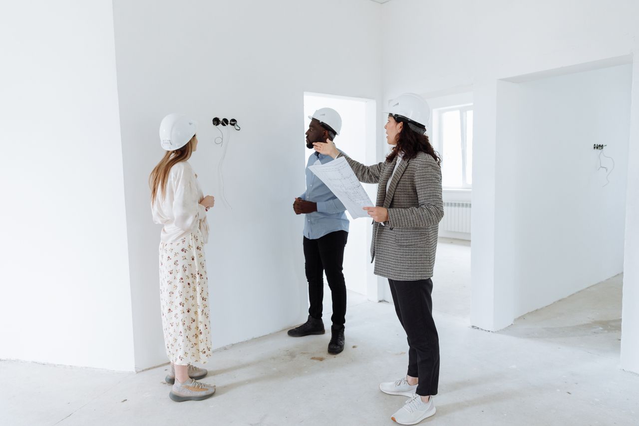 gallery-01 Three professionals discuss design plans inside a new house wearing hard hats.